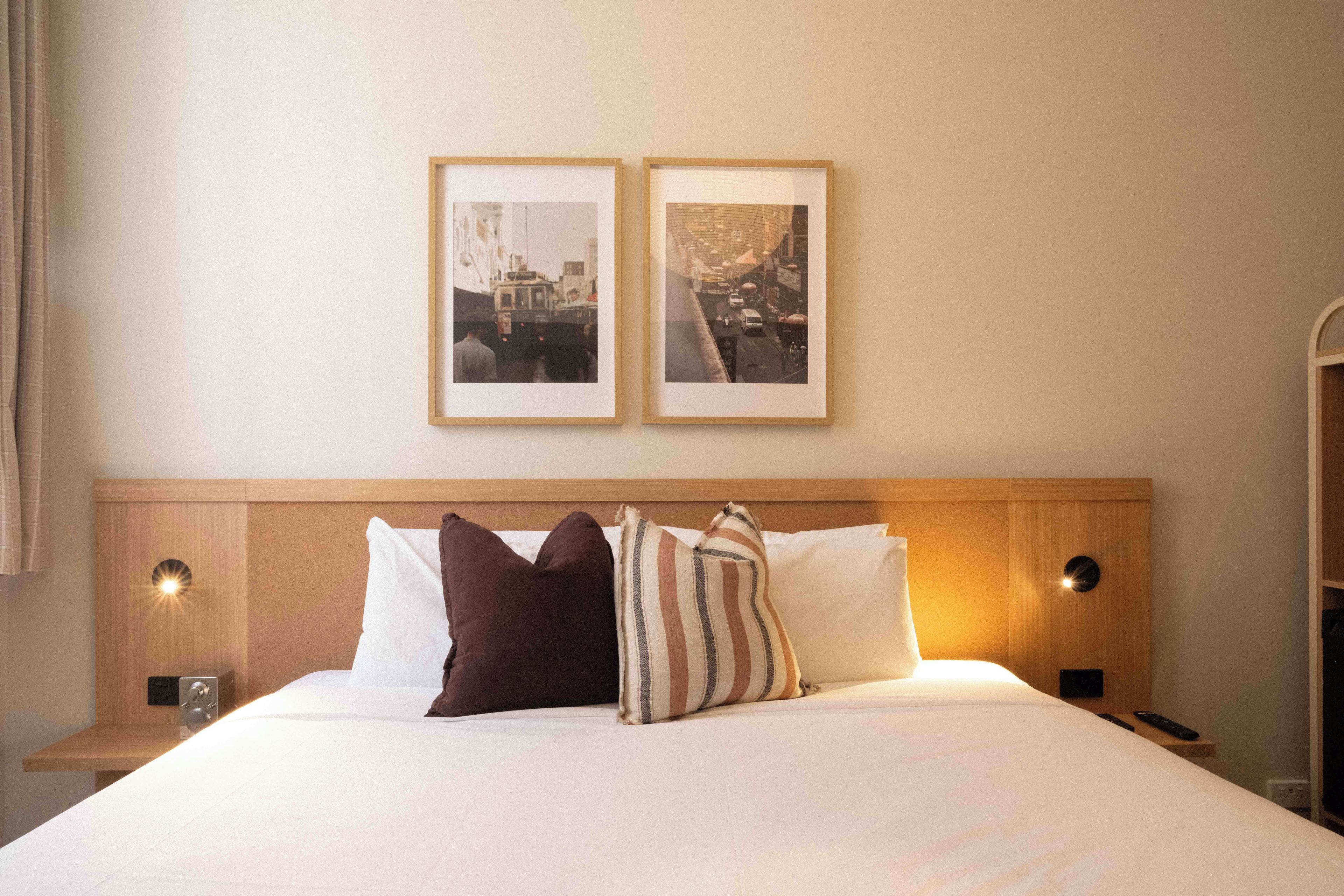 Una habitación de hotel con una cama, dos cuadros en la pared y una mesita de noche con una lámpara.