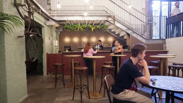 Un restaurante con zona de bar, taburetes de madera y una escalera.