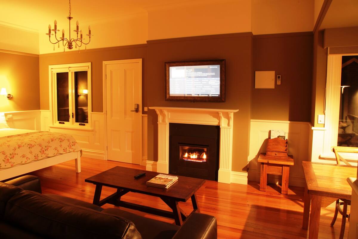 A cozy living room with a fireplace, a television mounted above it, a comfortable sofa, and a dining area with a table and chairs.