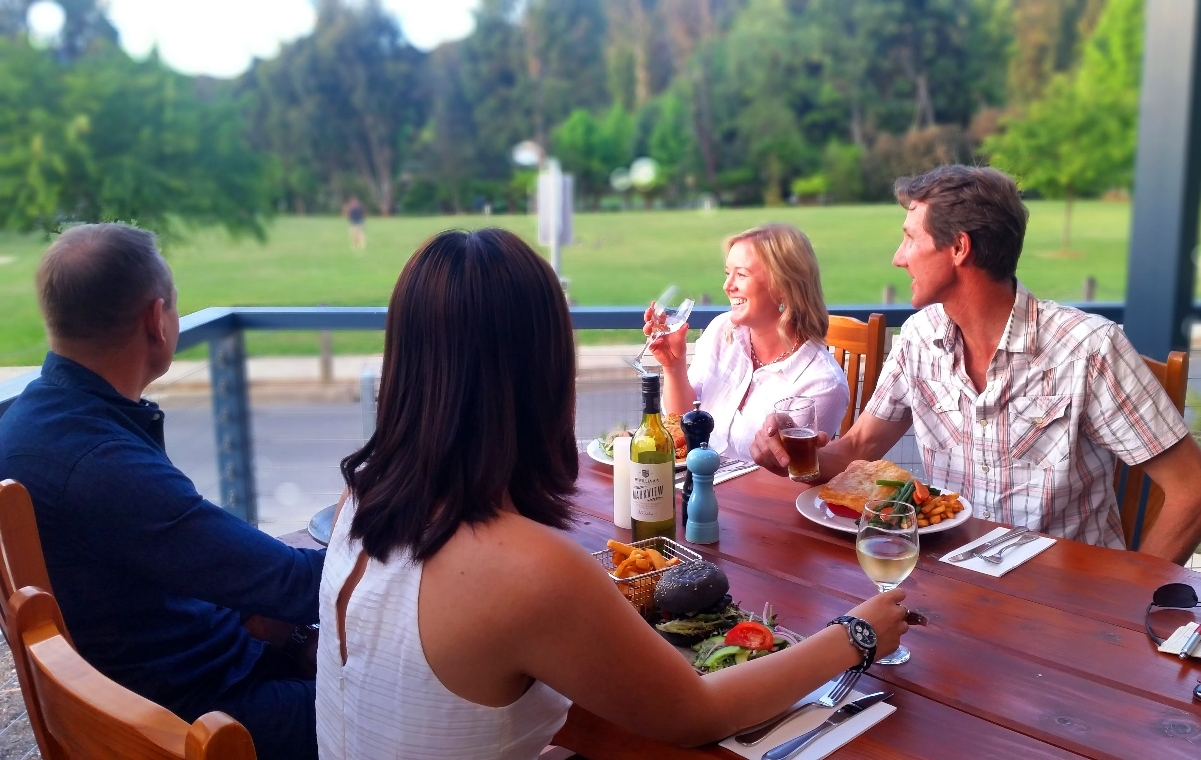 Un groupe de personnes est assis à une table en plein air, devant un espace verdoyant.