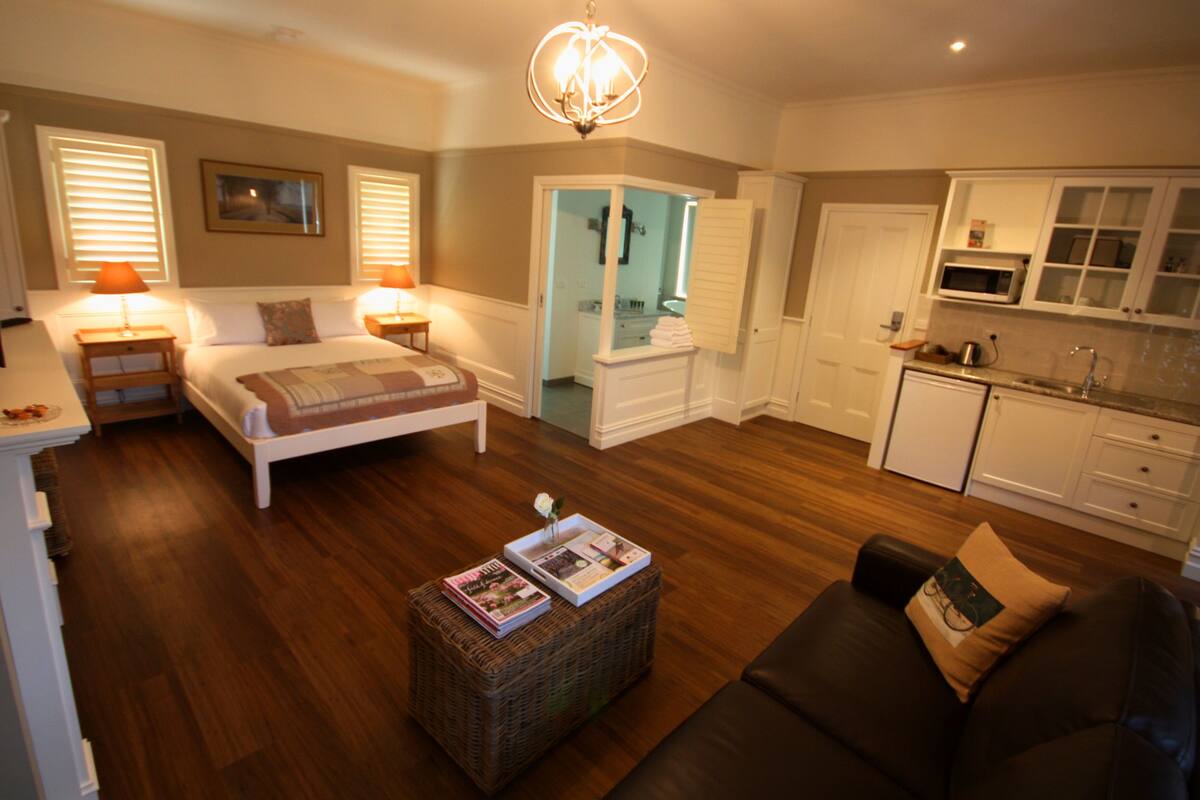 A bedroom with a bed, bedside tables, a nightstand, a reading chair, a small table with magazines, and a large mirror.