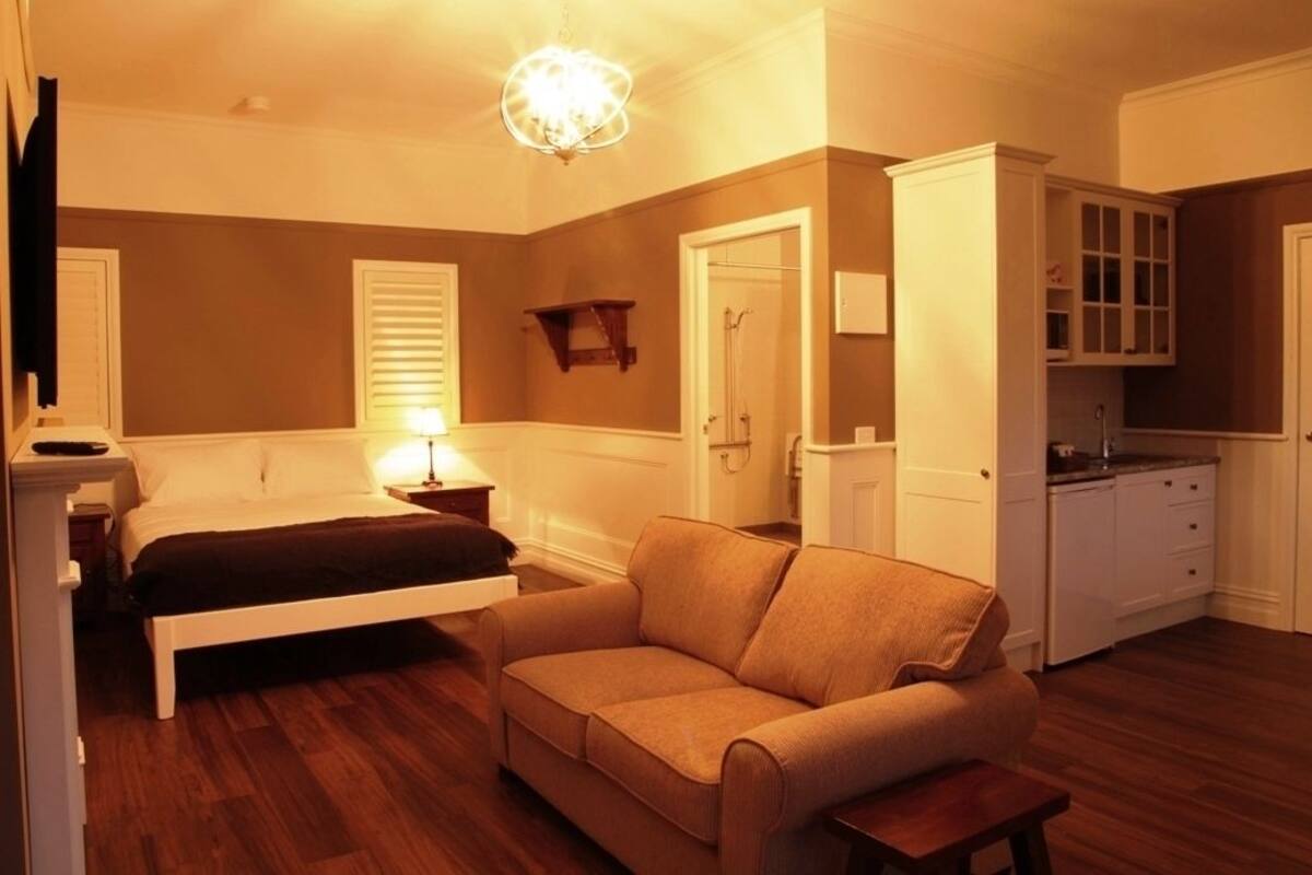 A bedroom with a bed, a sofa, a nightstand, a lamp, a wardrobe, and a small table.