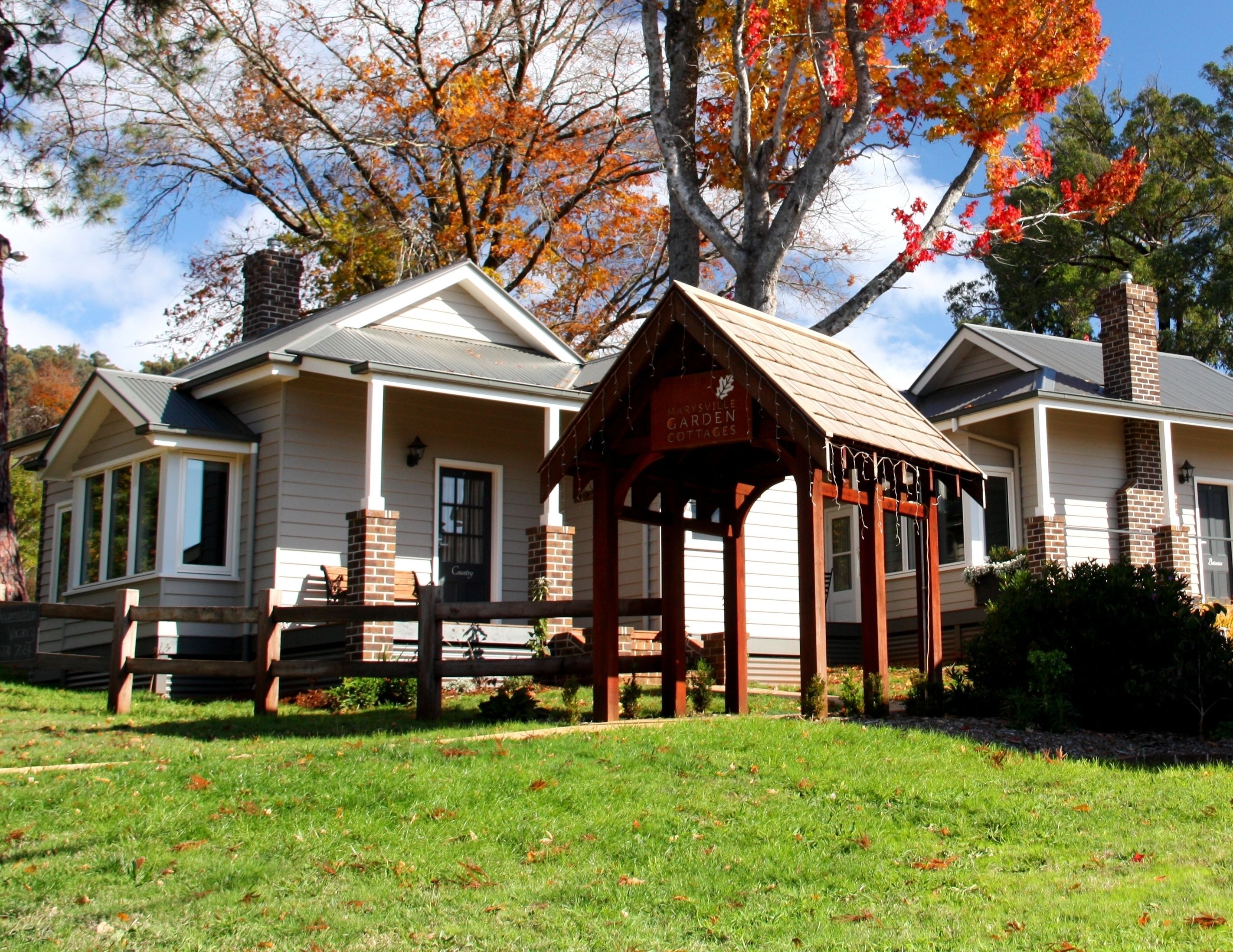 A row of cottages with a wooden fence in front, a sign for Marville Garden Cottages, and a tree with autumn leaves in the background.