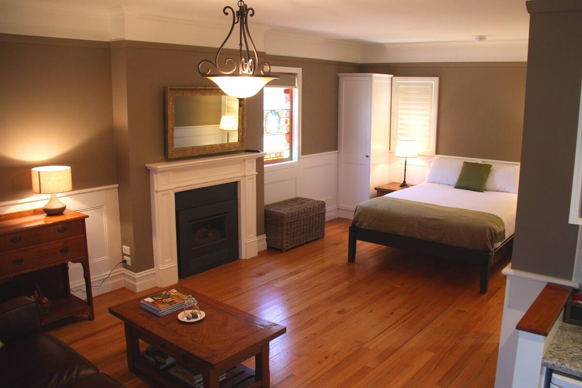 A bedroom with a bed, a nightstand, a dresser, a fireplace, and a window with blinds.