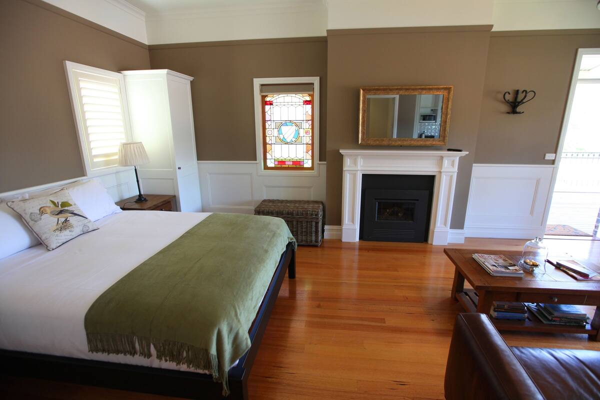 A bedroom with a bed, a fireplace, a mirror, and a window with stained glass.