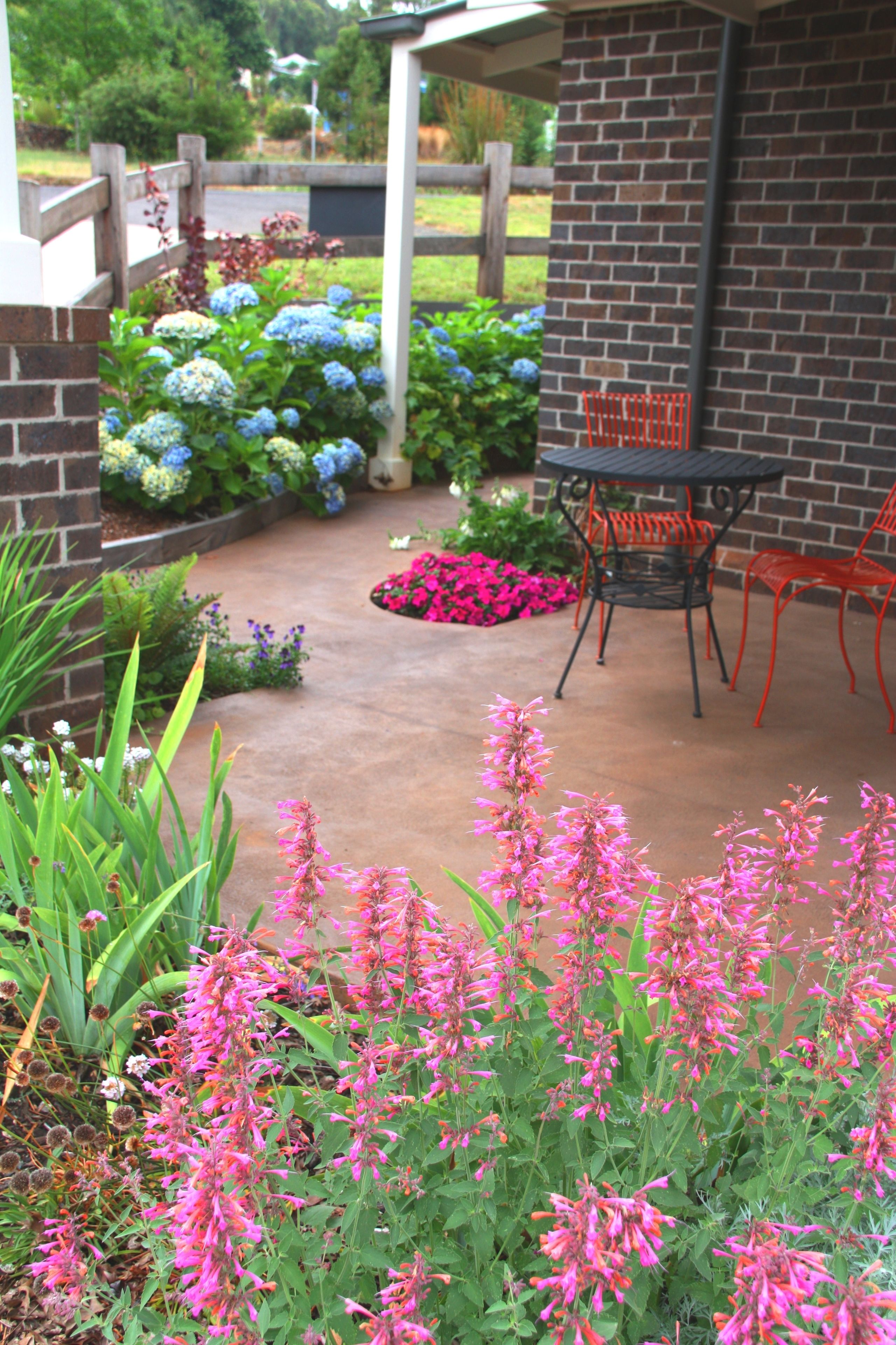 A patio with a brick wall, outdoor chairs, and a variety of flowers.
