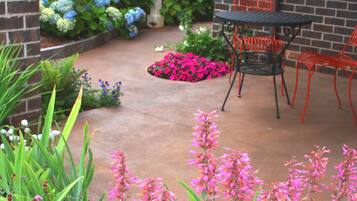 A patio with a brick wall, outdoor chairs, and a variety of flowers.