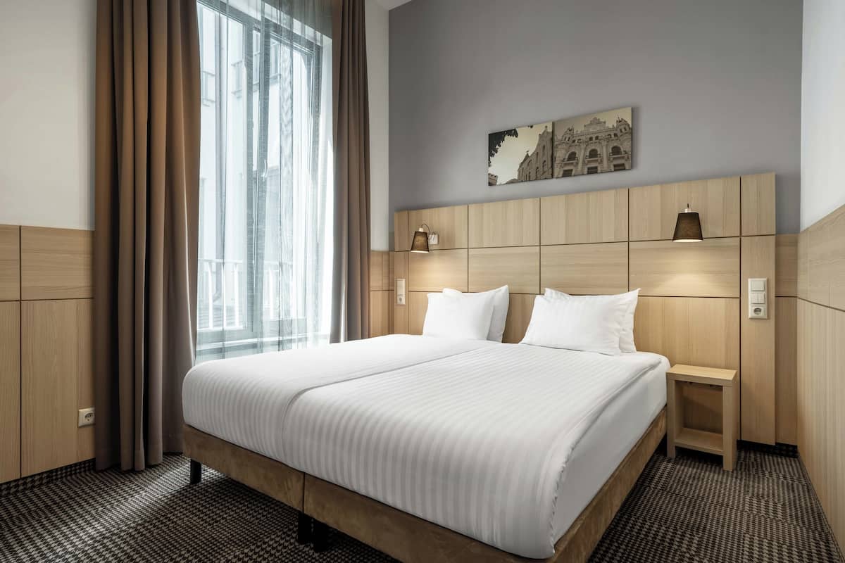 Hotellihuone, jossa on suuri sänky, yöp öytä, lamppu ja taulu seinällä.