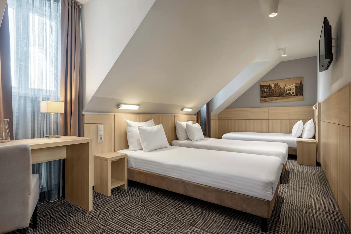 Hotellihuone, jossa on kaksi sänkyä, työpöytä, lamppu ja taulu seinällä.
