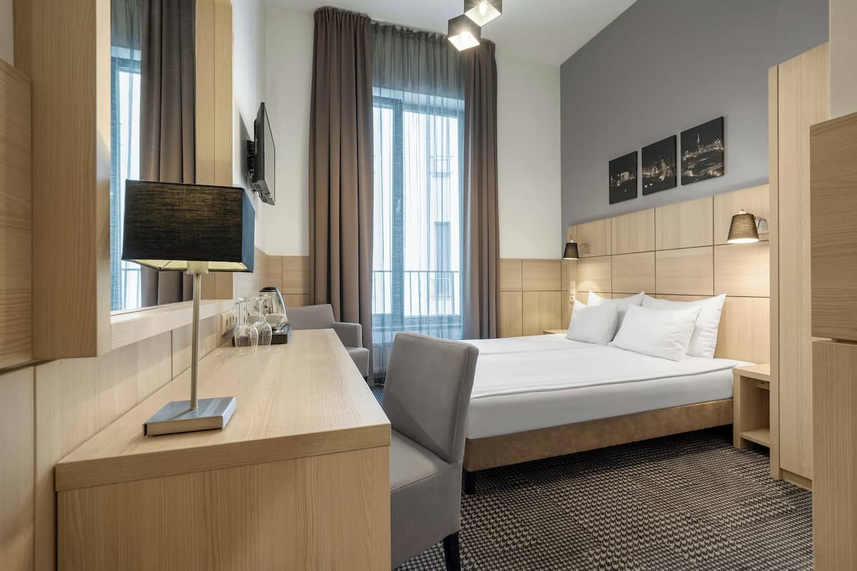 Hotellihuone, jossa on sänky, työpöytä, tuoli ja suuri ikkuna, jossa on verhot.