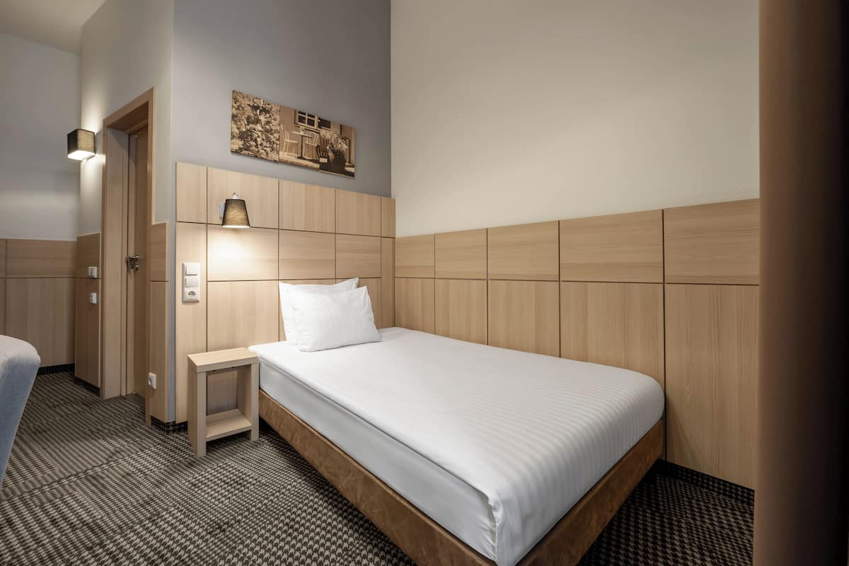 Hotellihuone, jossa on sänky, yöpöytä, seinään kiinnitetty lamppu ja taulu sängyn yläpuolella.