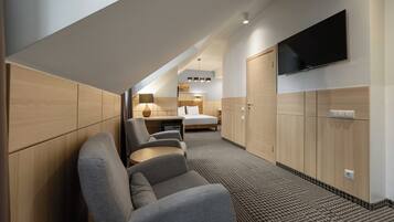 A hotel room with a sofa, a bed, a TV, and a desk with a lamp.