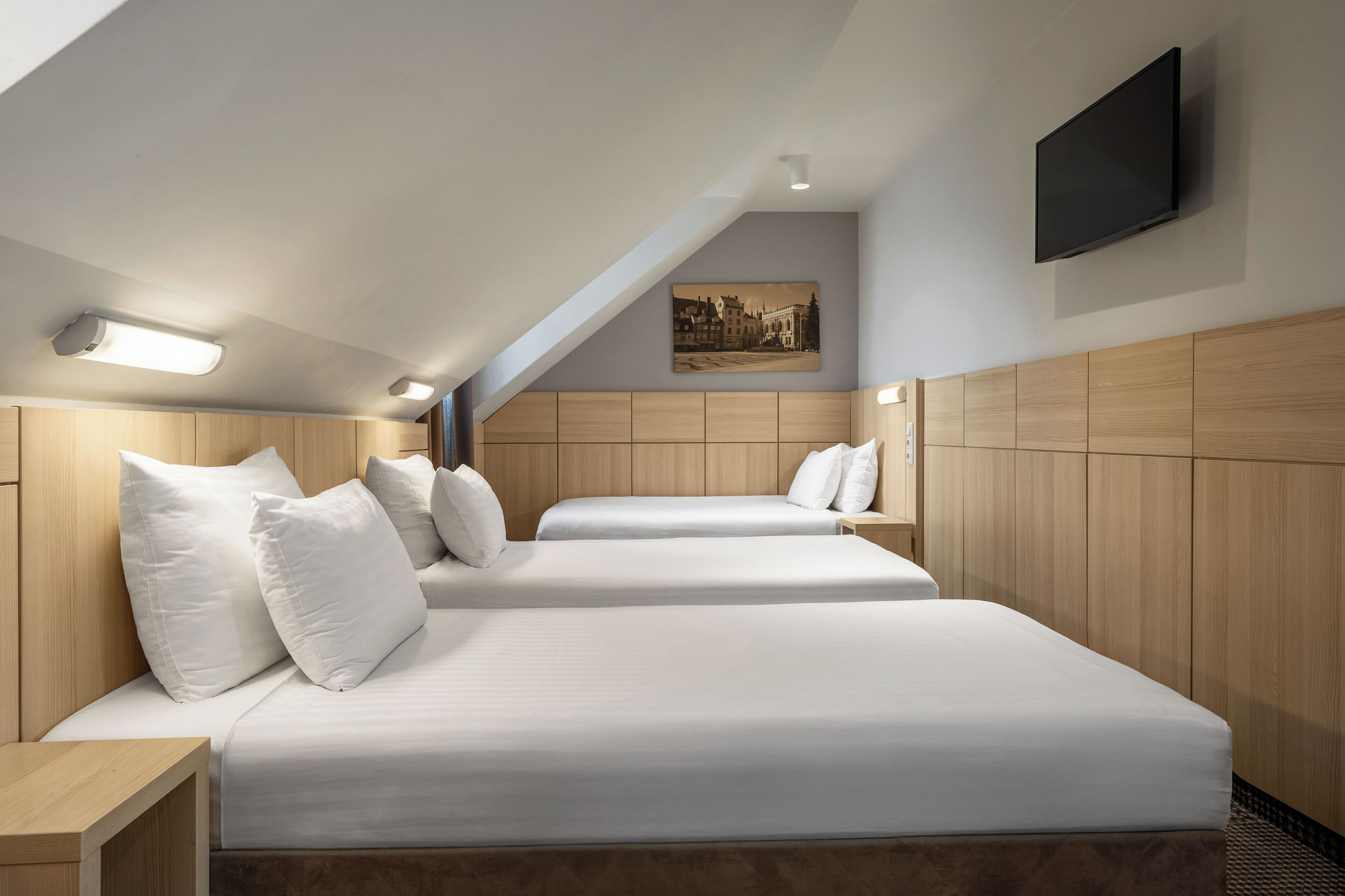 Habitación de hotel con dos camas, cabeceros de madera, un televisor de pantalla plana y una lámpara en el techo.