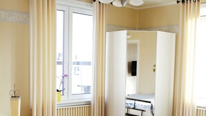 Une chambre à coucher avec un lit, une fenêtre avec des rideaux, un radiateur et un miroir.