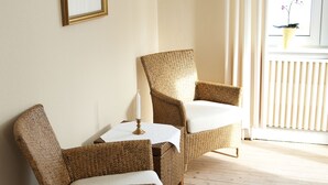 Une pièce comprenant deux fauteuils en osier, une petite table et un tableau encadré accroché au mur.