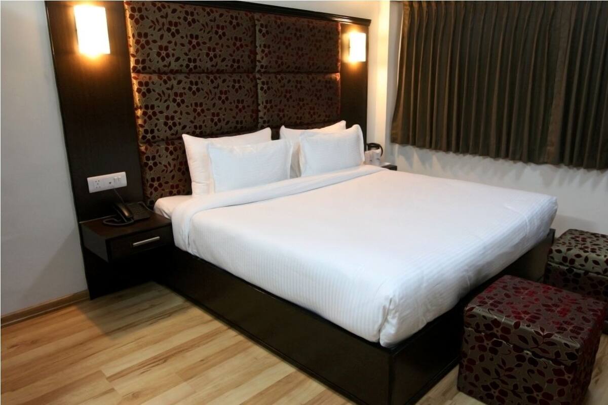 A neatly made bed with white linens, a dark headboard with a floral pattern, and two matching nightstands with a telephone and a lamp.