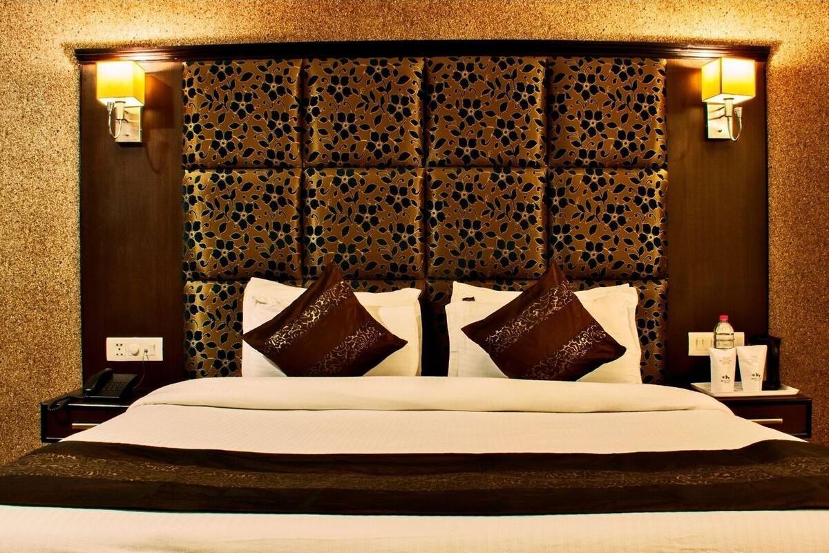 A hotel room with a large bed, a headboard with a leaf pattern, two bedside lamps, and a nightstand with a bottle and a tissue box.