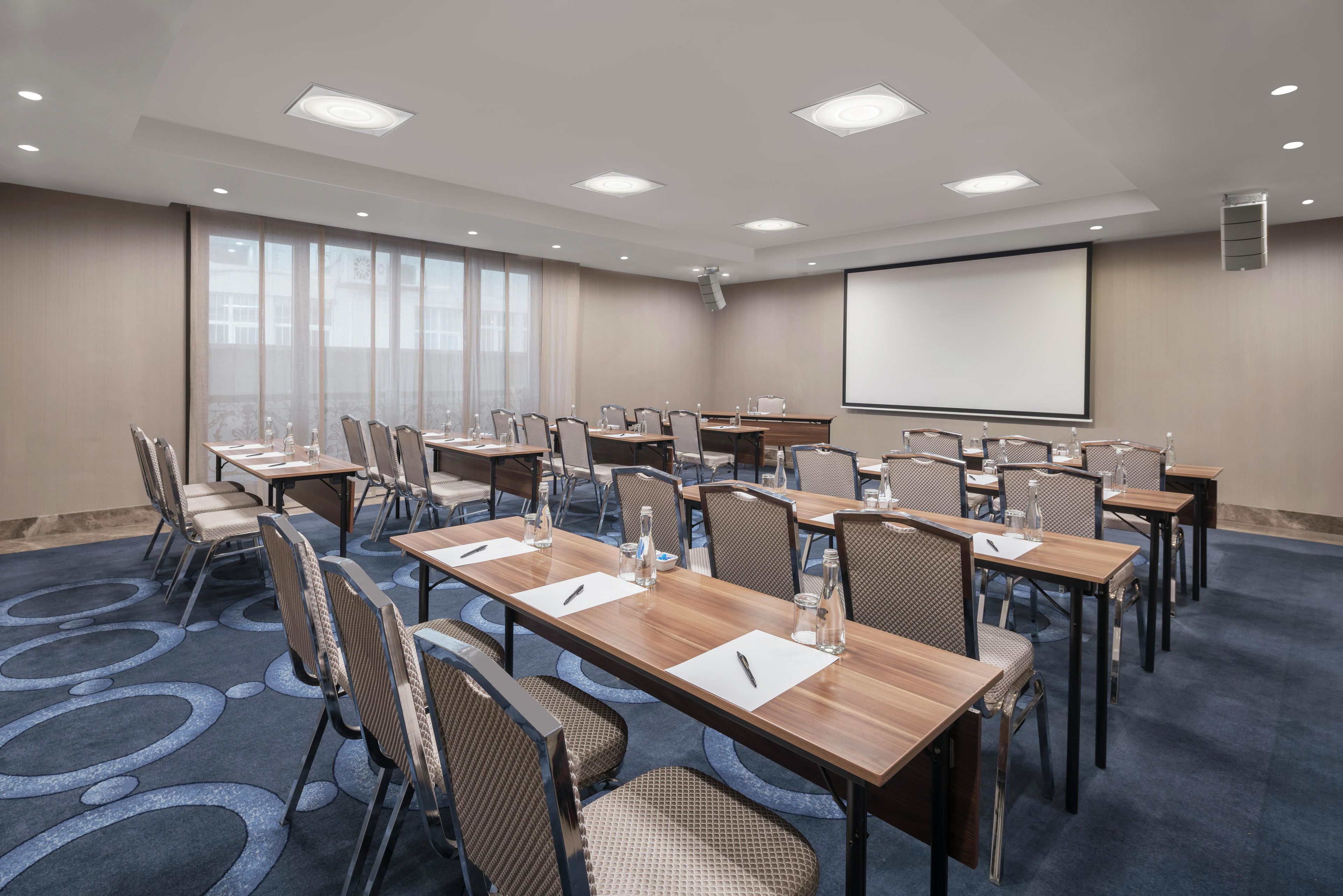 A conference room with multiple tables and chairs, a projector screen, and a large window.