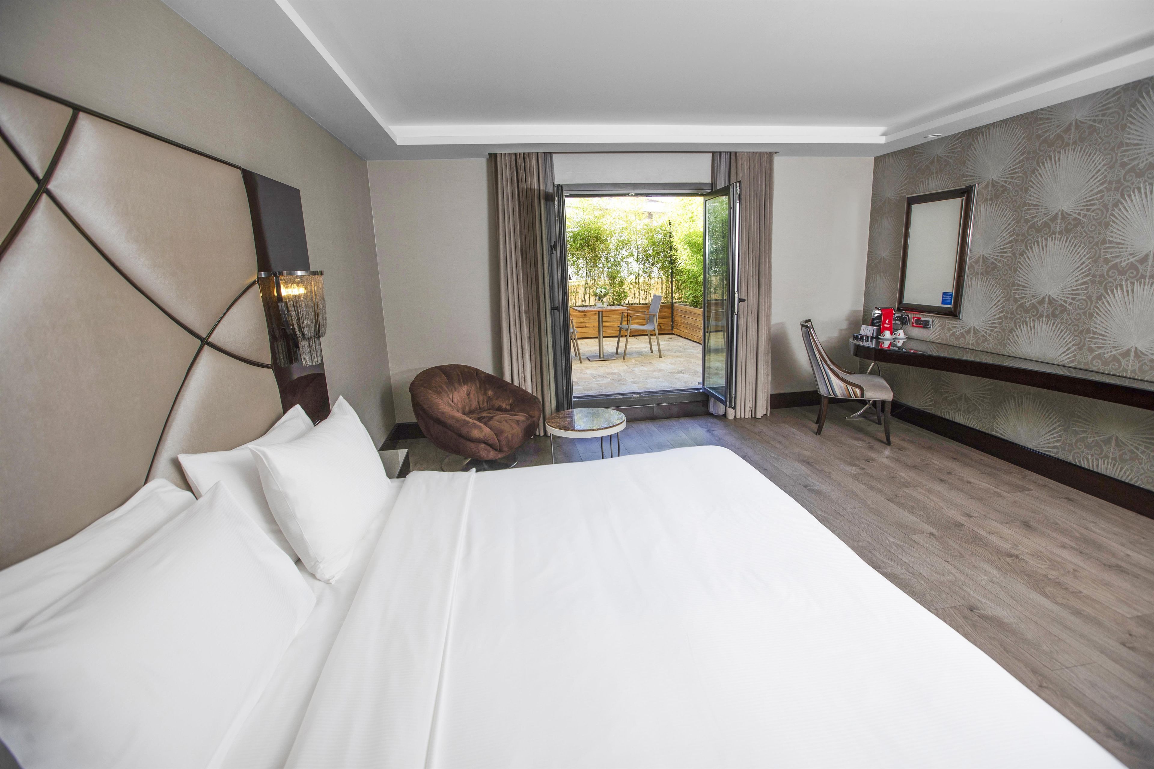 A hotel room with a large bed, a desk with a chair, a small table, and a view of the outdoors.