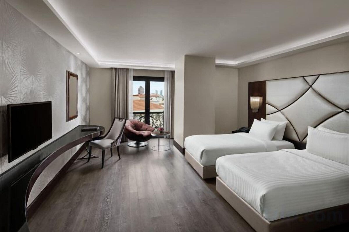 A hotel room with a TV, two beds, a desk, and a chair.