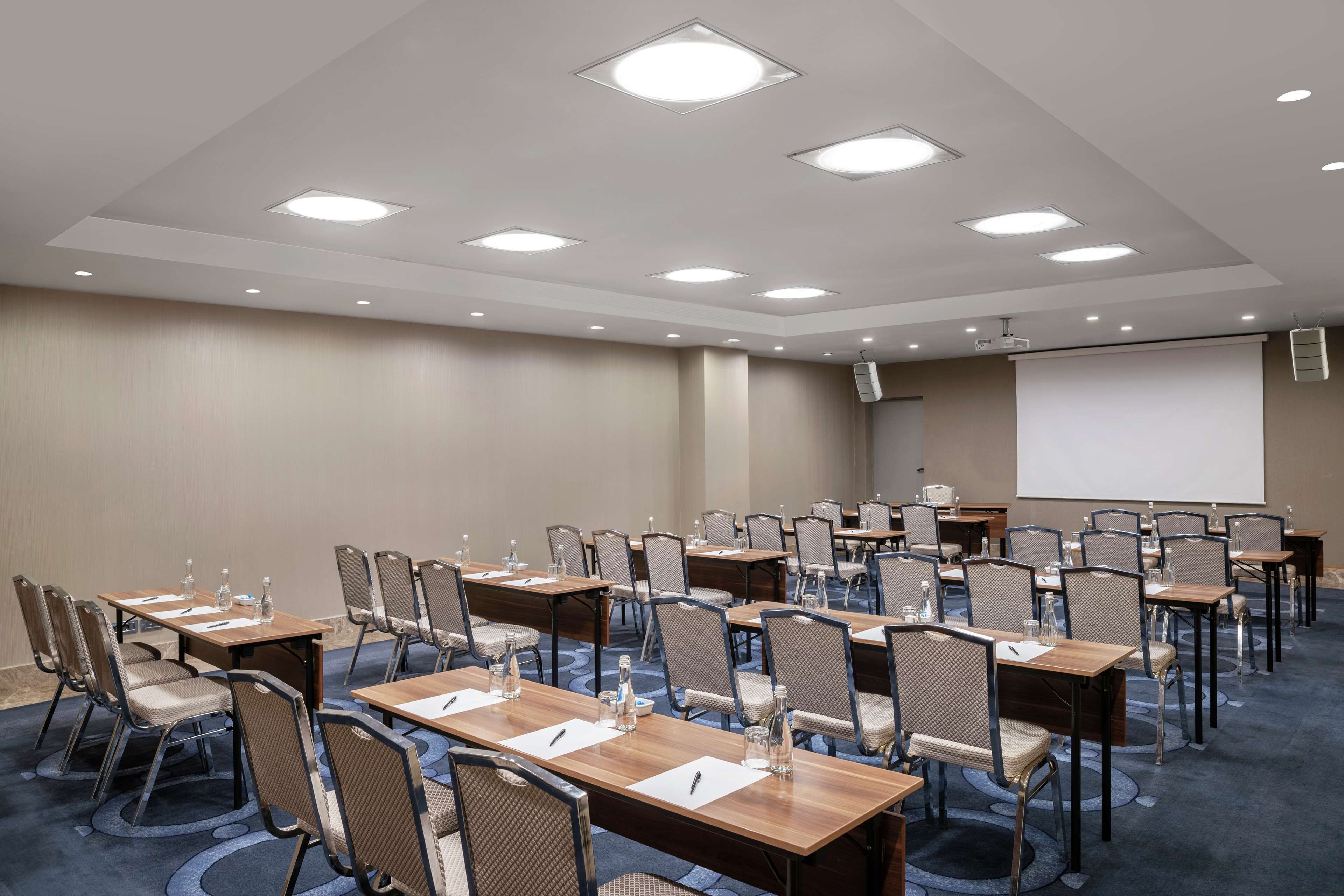 A conference room with multiple tables and chairs, equipped with projectors and screens.