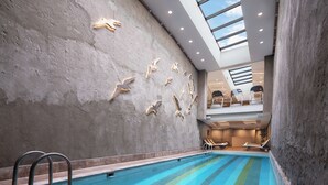 An indoor swimming pool with a concrete wall featuring bird sculptures, a skylight, and lounge chairs. - DoubleTree By Hilton Istanbul Gayrettepe (Istanbul)