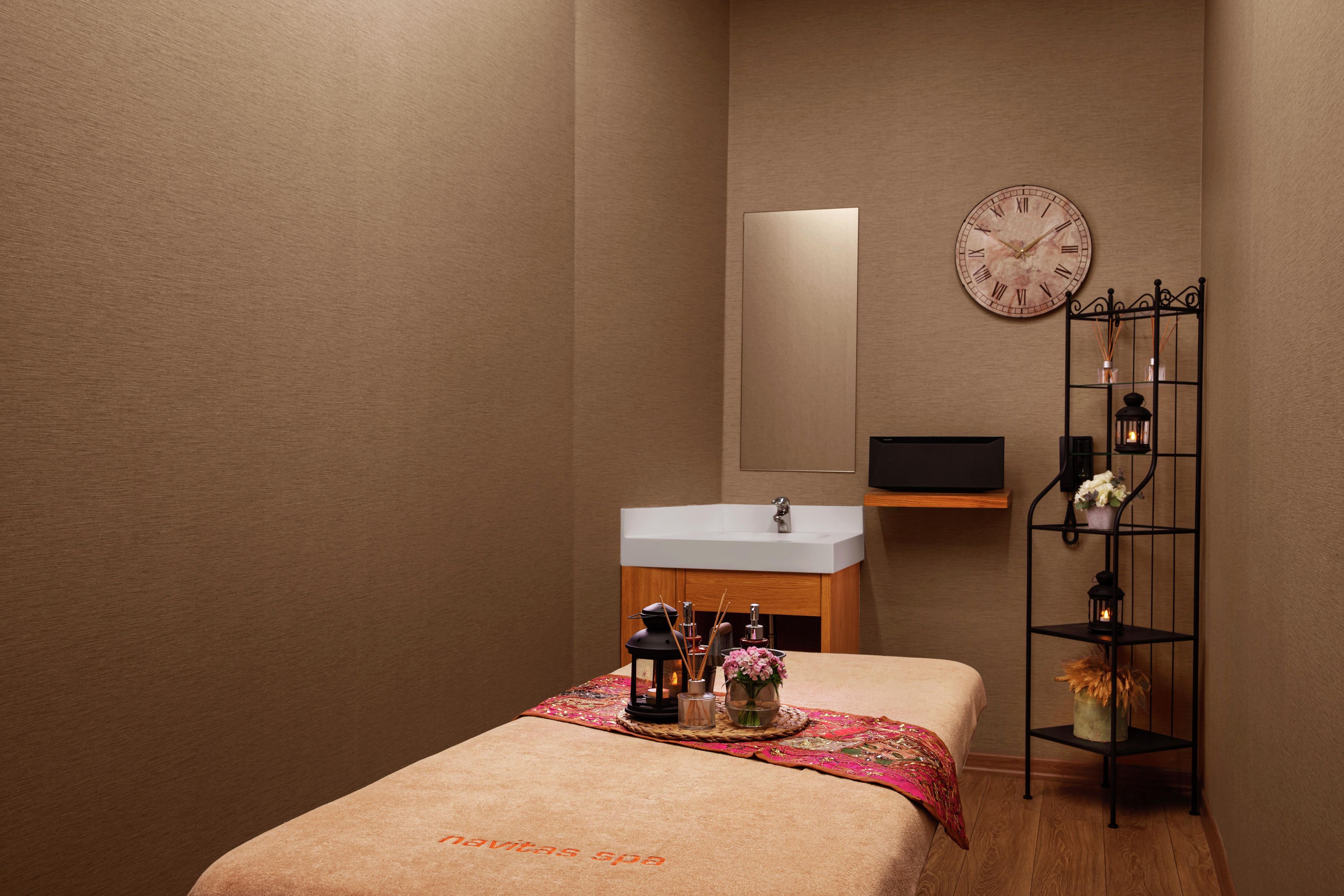 A small, cozy room with a bed, a bedside table with a lamp, a mirror, and a clock on the wall.