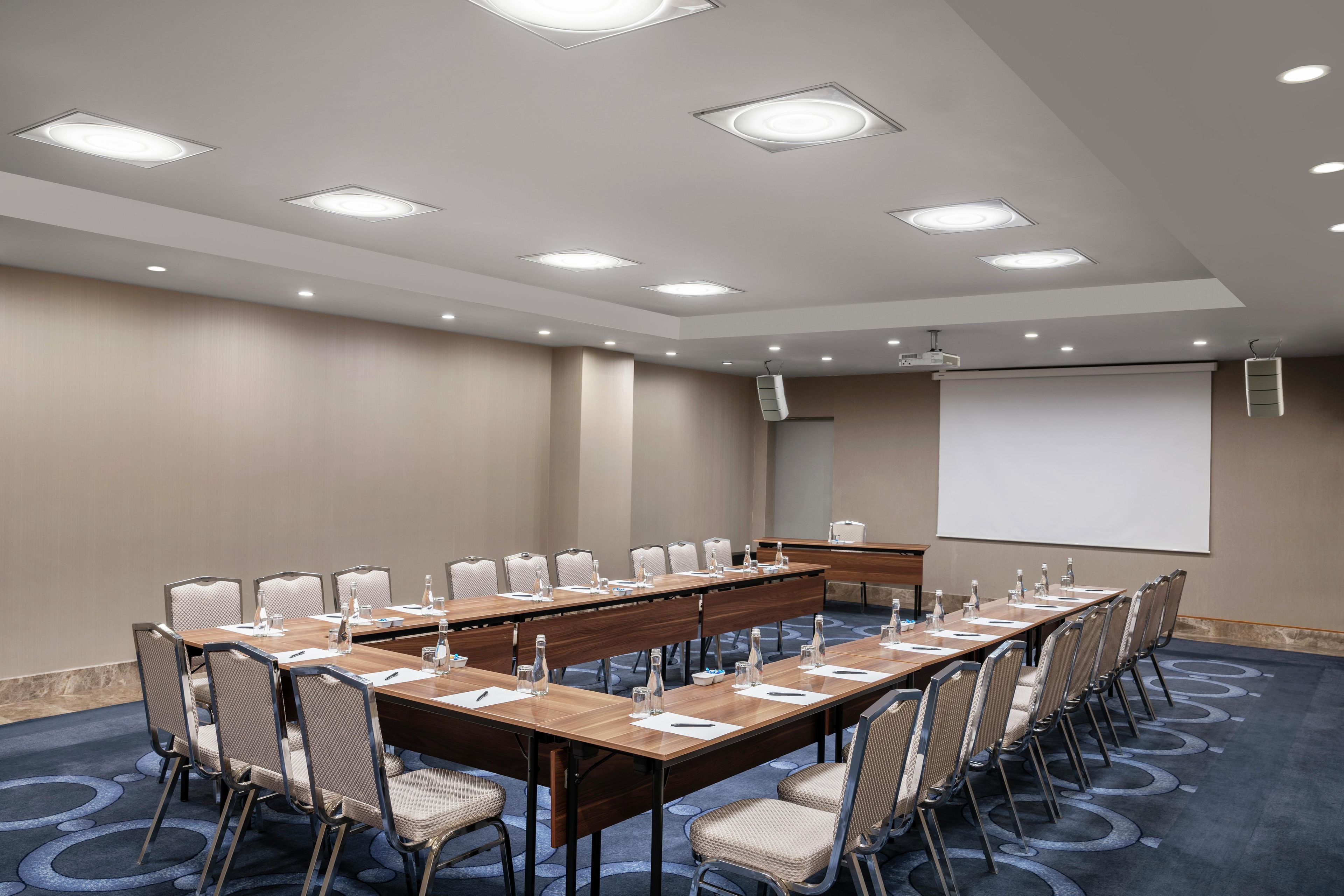 Un salón de conferencias con una larga mesa, sillas, una pantalla de proyector y una pizarra.