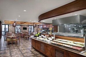 A buffet area with a variety of food options, a kitchen in the background, and a seating area with tables and chairs. - DoubleTree By Hilton Istanbul Gayrettepe (Istanbul)