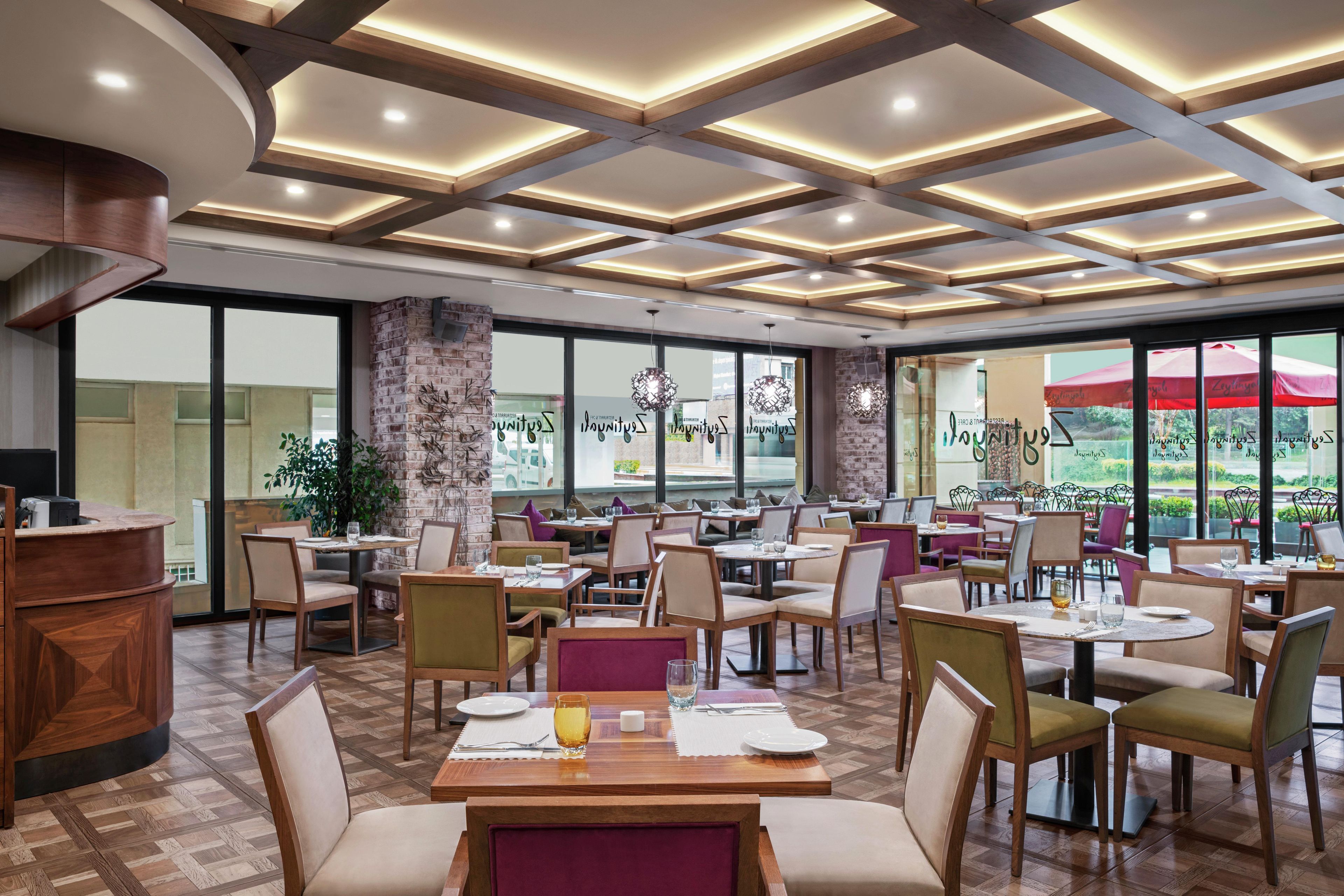 Ein Restaurant mit mehreren Tischen und Stühlen, einer Ziegelwand und großen Fenstern mit Blick ins Freie.