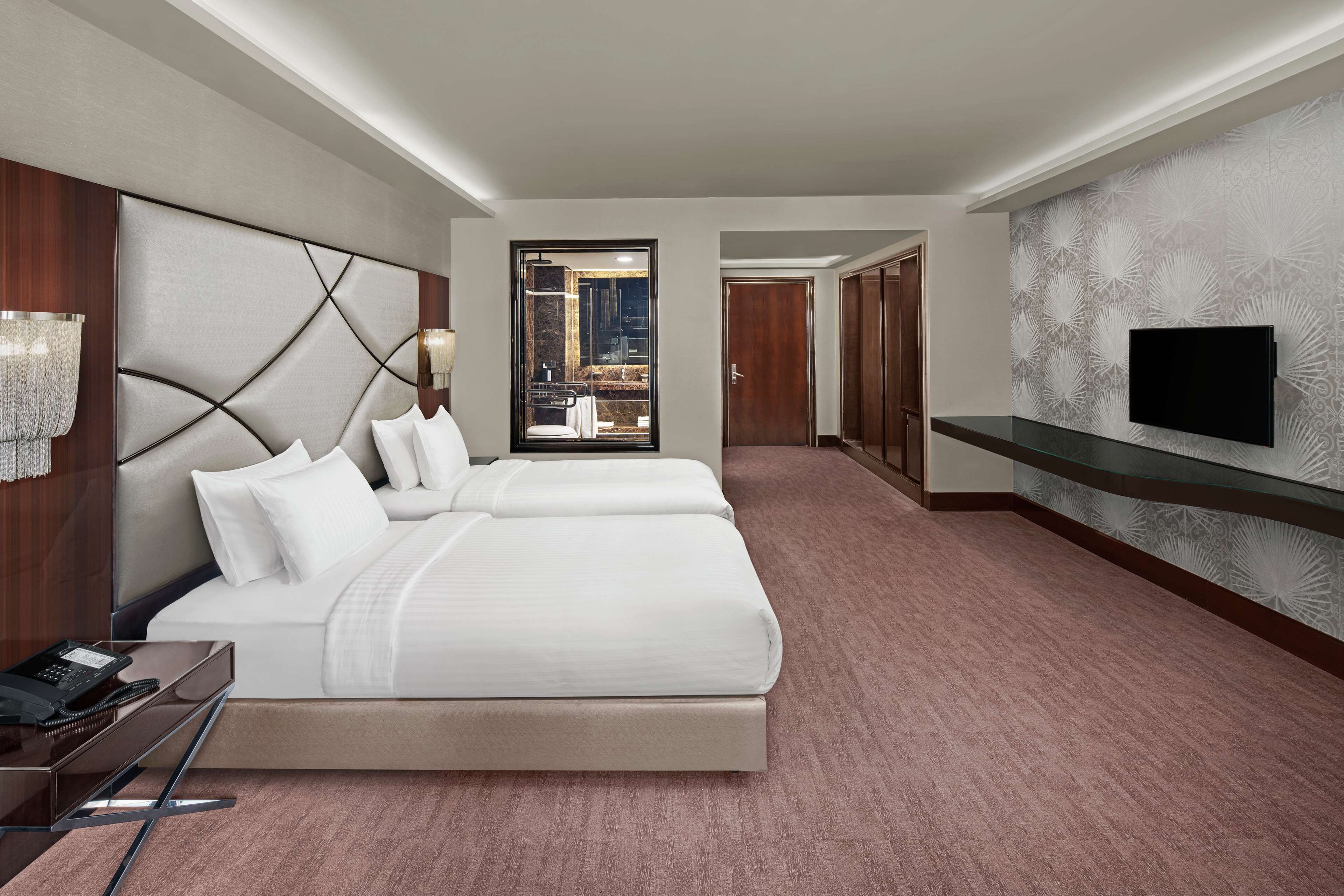 A hotel room with a large bed, bedside tables, a TV, and a view through a glass door.