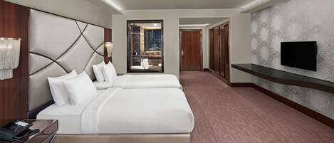 A hotel room with a large bed, bedside tables, a TV, and a view through a glass door.