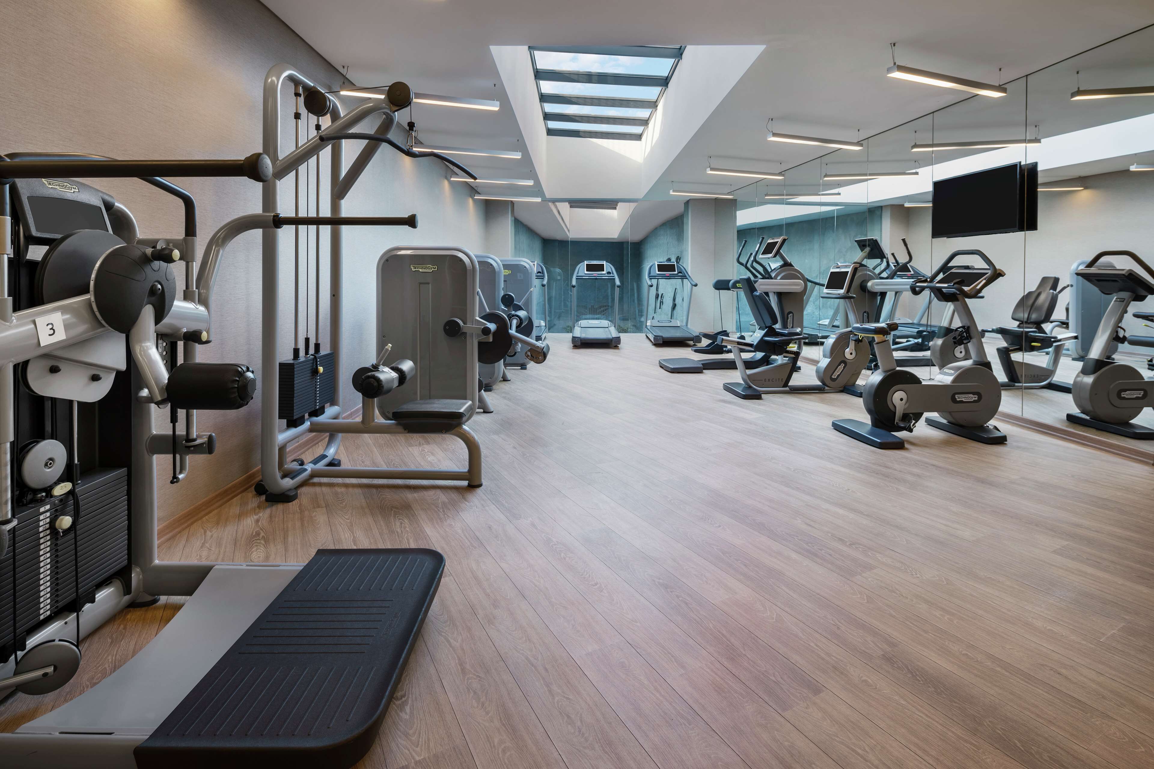 A modern gym with various exercise machines, a skylight, and a large mirror.