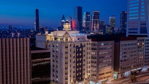 A hotel with a classic architectural style, featuring a prominent dome and a marquee sign. It is surrounded by modern high-rise buildings and a busy road with light trails. - DoubleTree By Hilton Istanbul Gayrettepe (Istanbul)