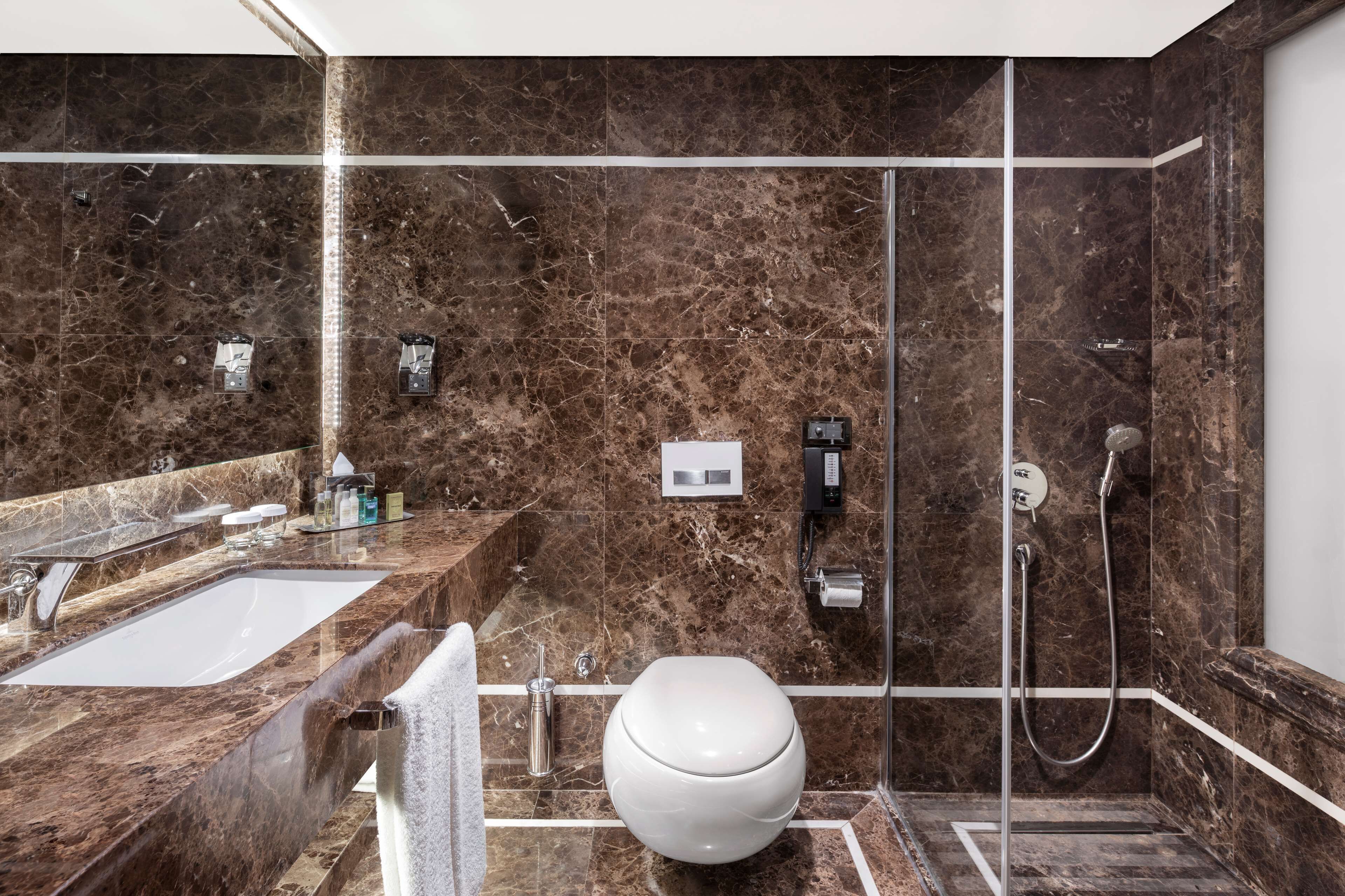 A modern bathroom with a marble sink, a toilet, and a glass-enclosed shower.