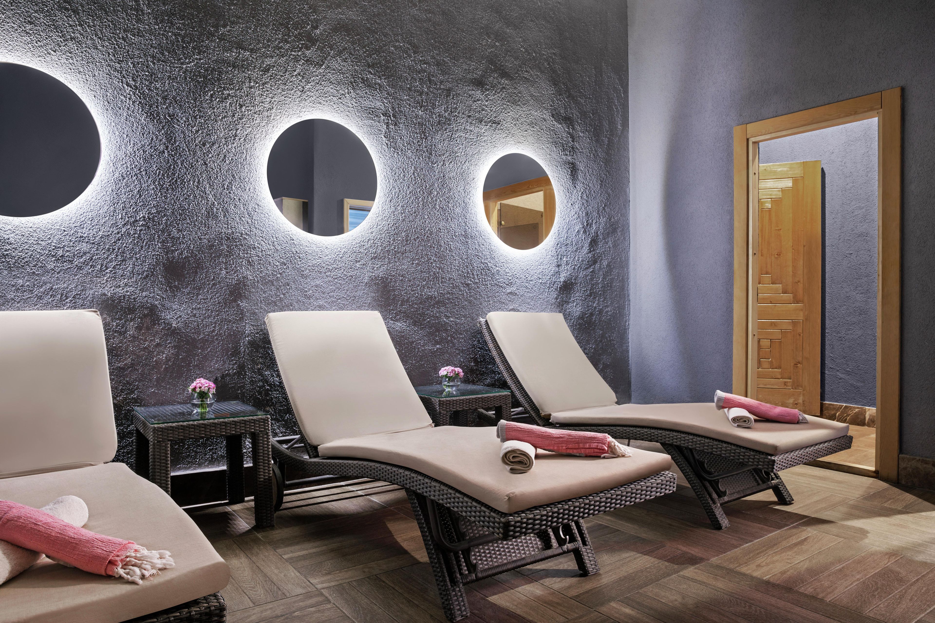 Un cuarto de spa con tres sillones reclinables, una mesita con un florero y una puerta de madera.