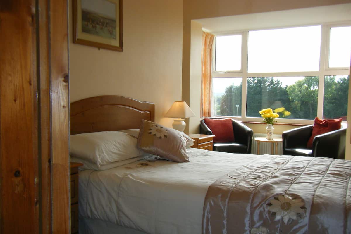 Une chambre d’hôtel avec un lit, une chaise, une table et une fenêtre avec des rideaux.