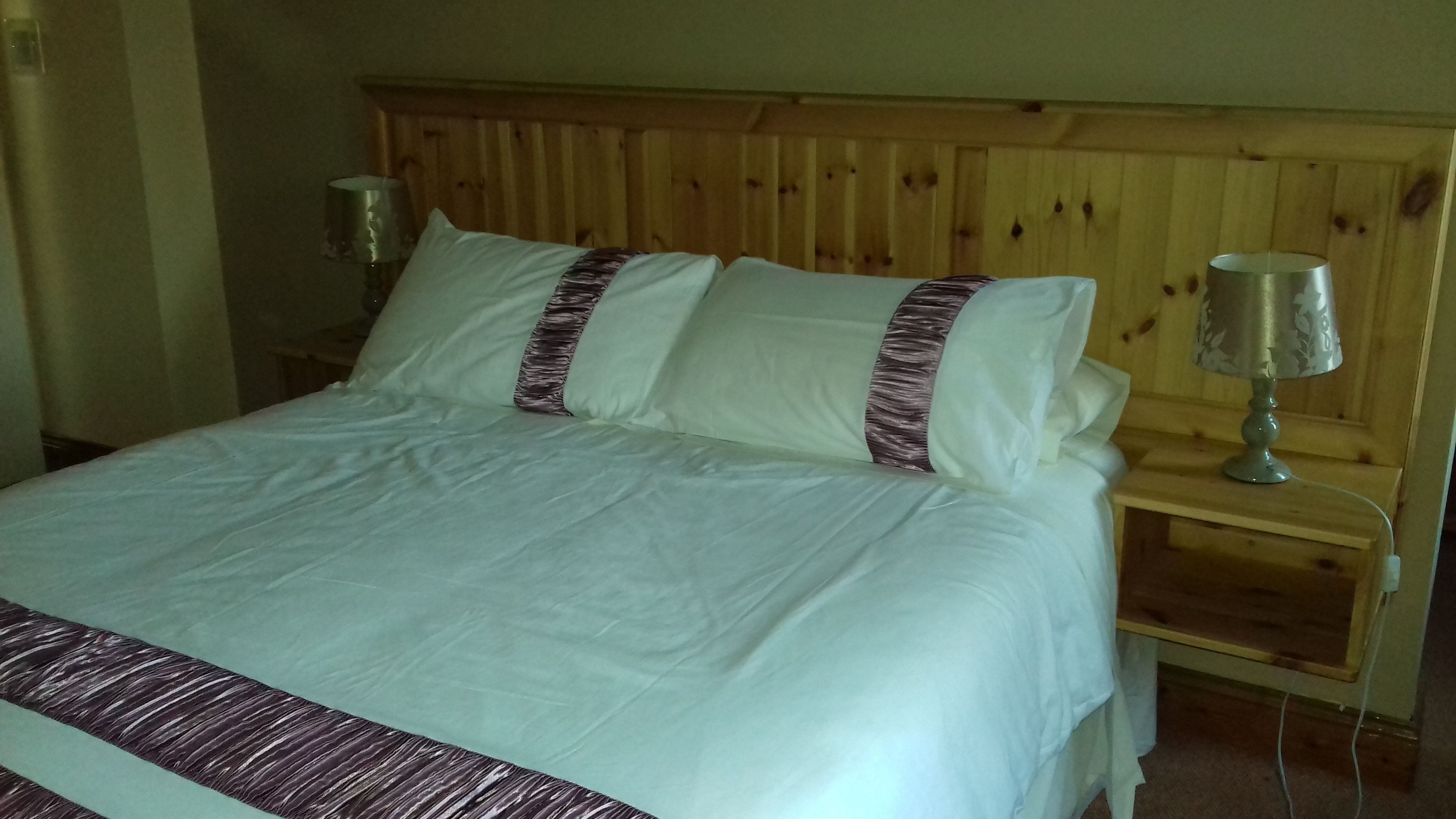 A bed with white bedding and two pillows, a wooden headboard, and two bedside lamps.