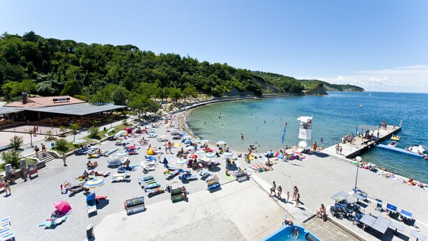 Une plage avec des chaises longues, des parasols et une jetée qui s’avance dans l’eau.