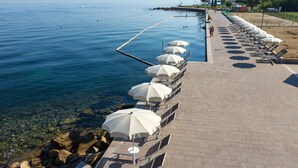 Une promenade en bord de mer, avec des chaises longues et des parasols, une vue dégagée sur l’eau et une côte rocheuse.
