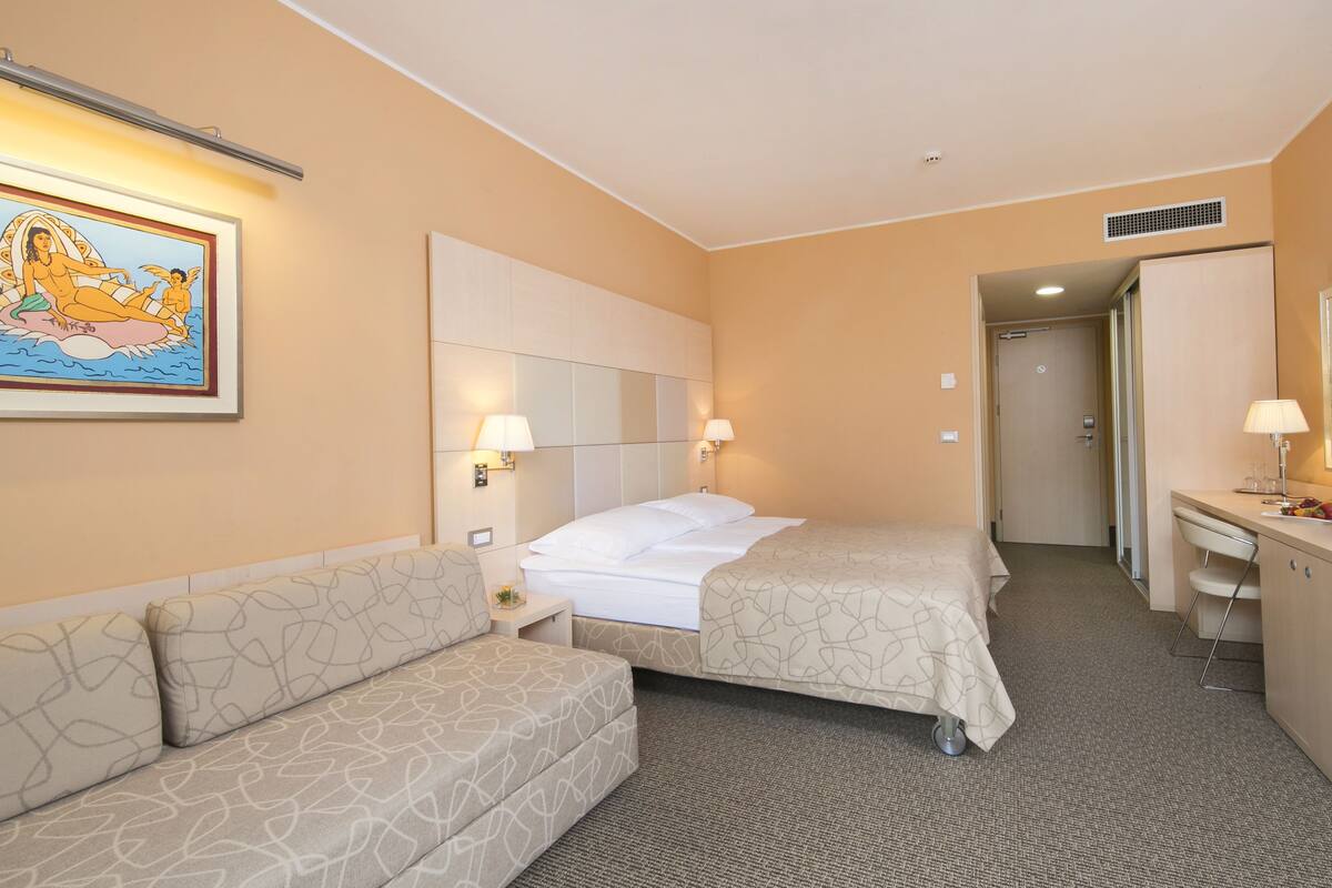 Une chambre d’hôtel avec deux lits, un canapé, un bureau et un miroir.