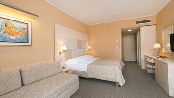 A hotel room with two beds, a sofa, a desk, a mirror, and a wall-mounted artwork.