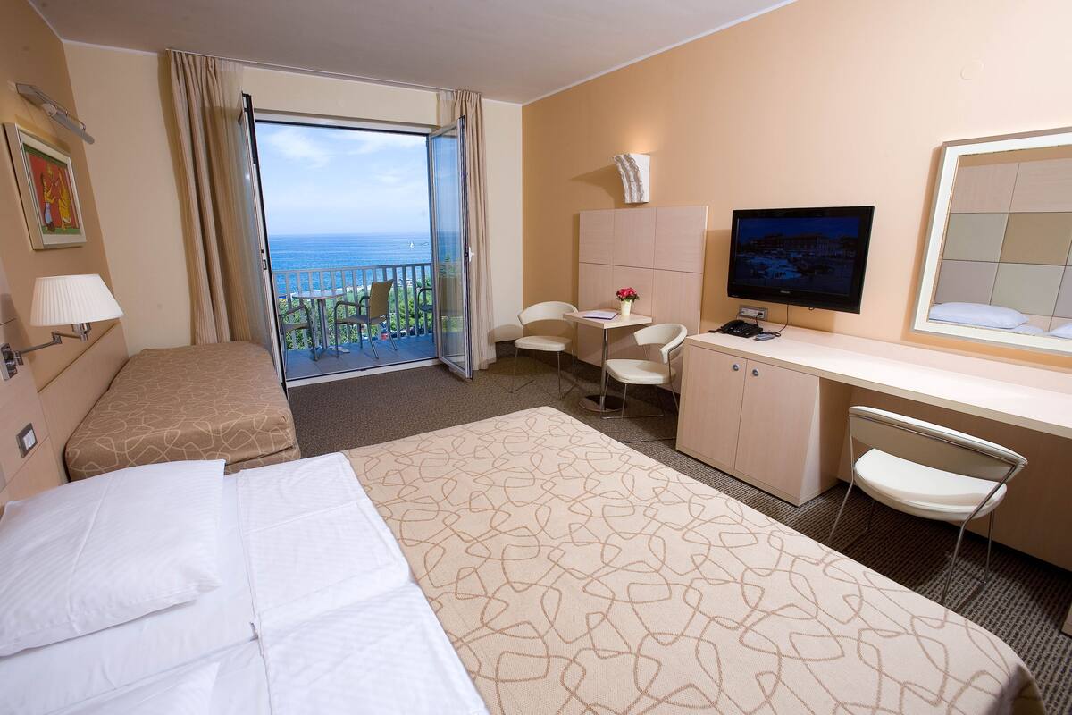 Une chambre d’hôtel comprenant un lit, un bureau, une chaise, une télévision et un balcon avec vue sur l’océan.