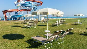 Relax in comfort with lounge chairs and umbrellas on the lush grass, overlooking the ocean and a vibrant water park.