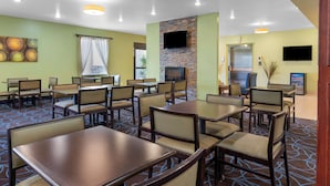 Un espace de restauration d’hôtel comprenant plusieurs tables et chaises, une cheminée, un téléviseur et un ascenseur.