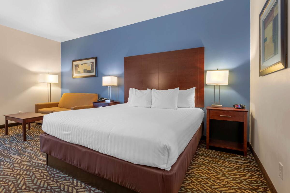 A hotel room with a large bed, a sofa, two bedside tables with lamps, and a patterned carpet.