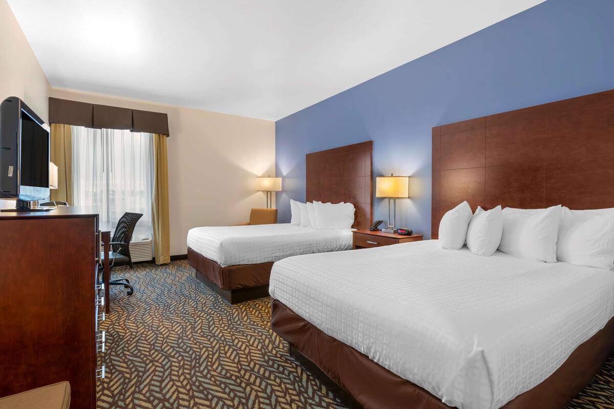 A hotel room with two beds, a desk, a TV, and a patterned carpet.