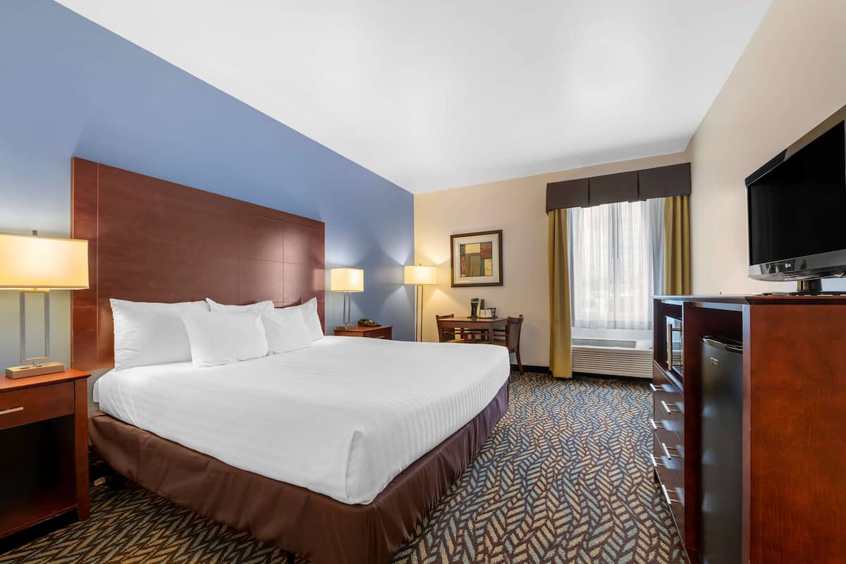 A hotel room with a large bed, two bedside lamps, a desk with a chair, a television, and a window with curtains.