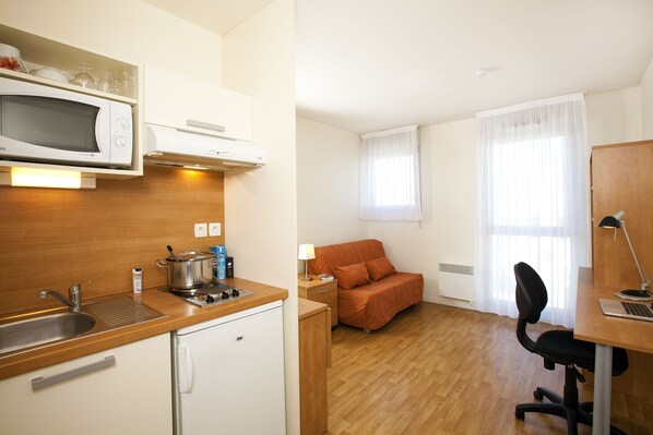 A compact kitchenette with a microwave, stove, and sink. A small refrigerator is also visible.
