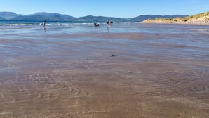 A beach with people walking and playing, and mountains in the background.